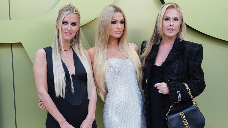 drei blonde Frauen, links in schwarzem Kleid, Mitte in weissem Kleid, recht in schwarzem Blazer. Frau rechts älter.
