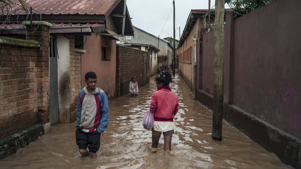 Zwei Menschen laufen in Antananarivo, Madagaskar durch kniehohes Wasser.