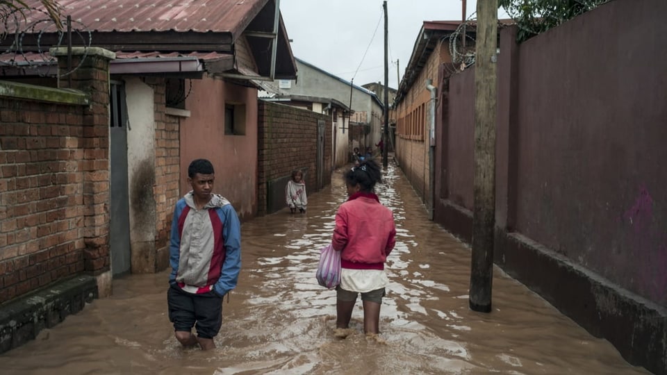 Kampf gegen die Wassermassen Zwei Menschen laufen in Antananarivo, Madagaskar durch kniehohes Wasser.