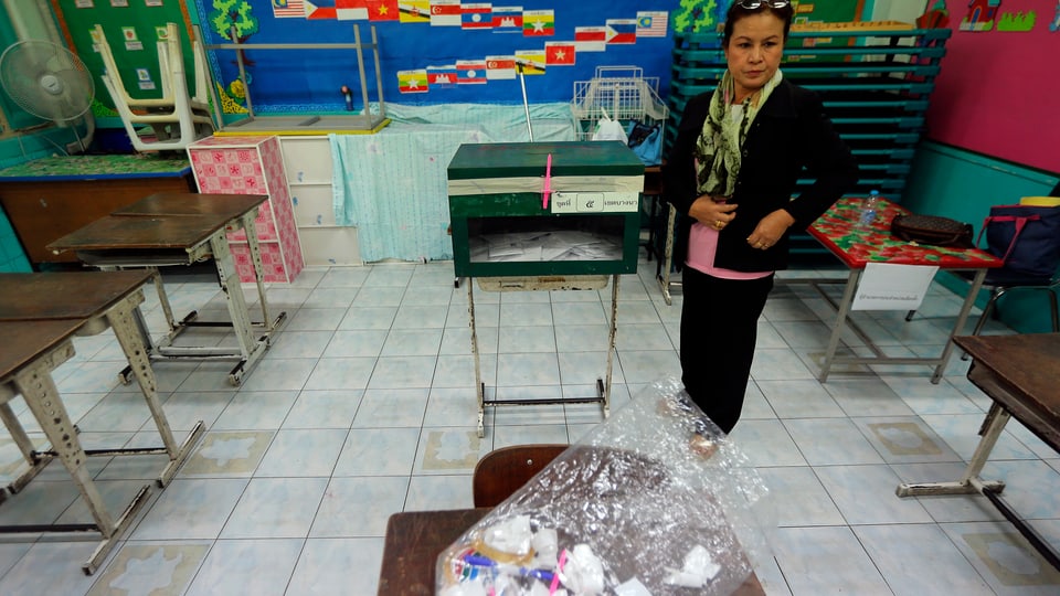 Eine thailändische Frau steht alleine in einem Wahllokal.