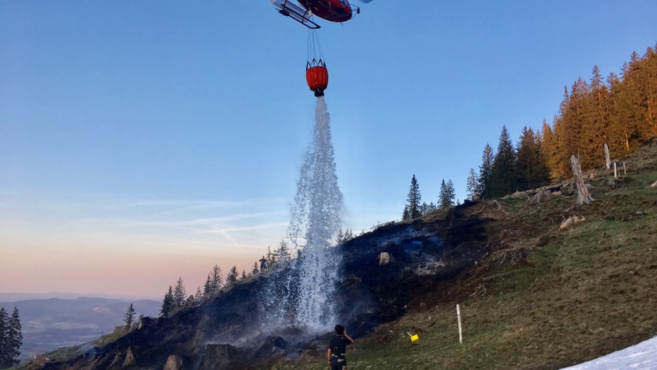 Helikopter lässt Wasser auf verbrannte Erde herunter