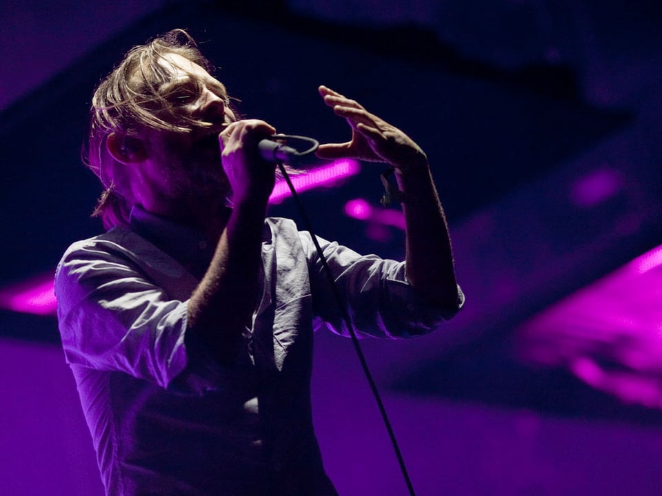 Der Sänger Thom Yorke singt in ein Mikrofon an einem Konzert.