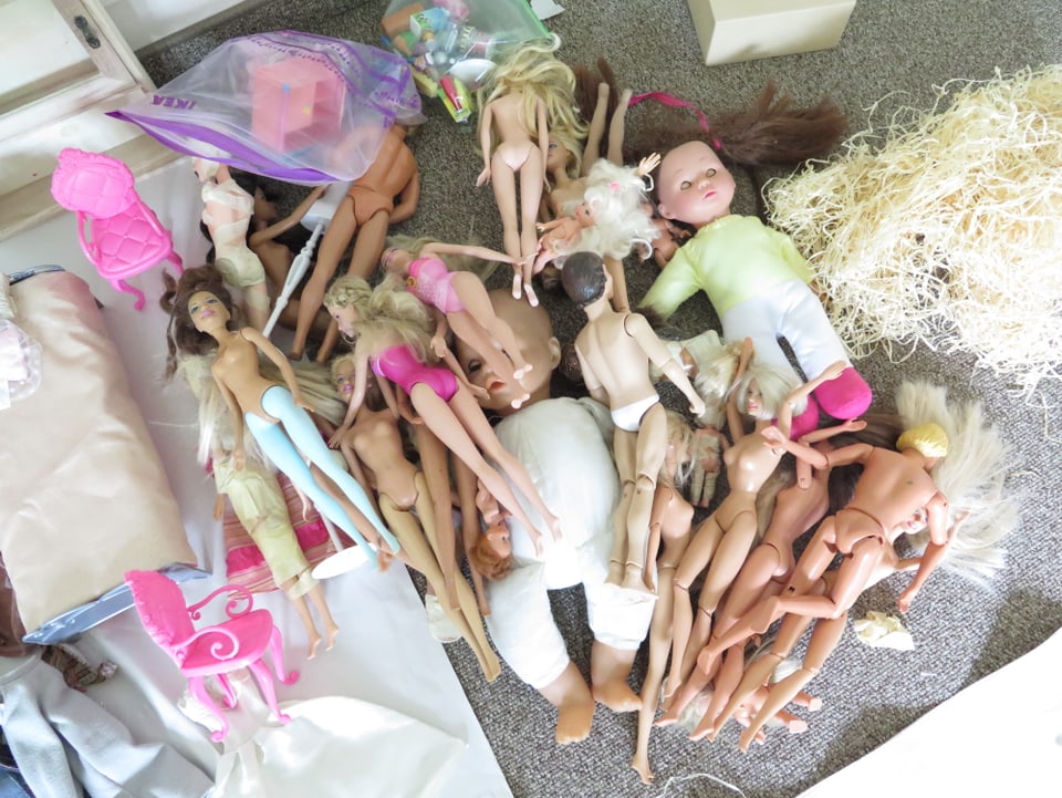 Am Boden liegen nackte Barbies und Puppen. 