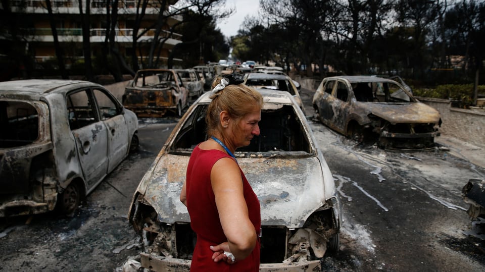 Frau steht vor verbrannten Autos, die durch ein Wildfeuer zerstört wurden