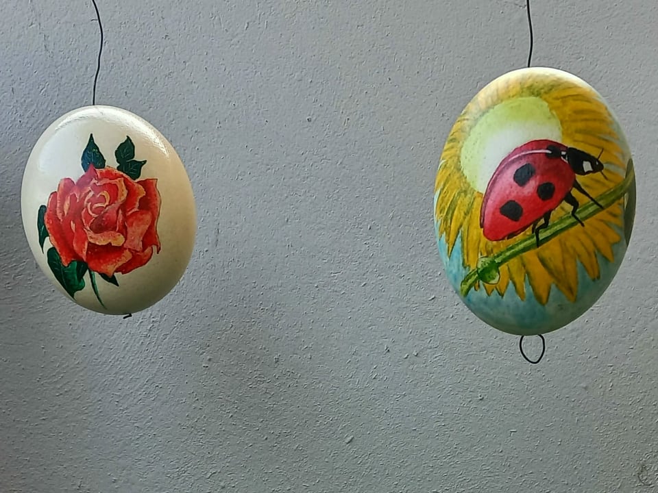 Zwei bemalte Eier, eines mit Rose und eines mit einem Marienkäfer.