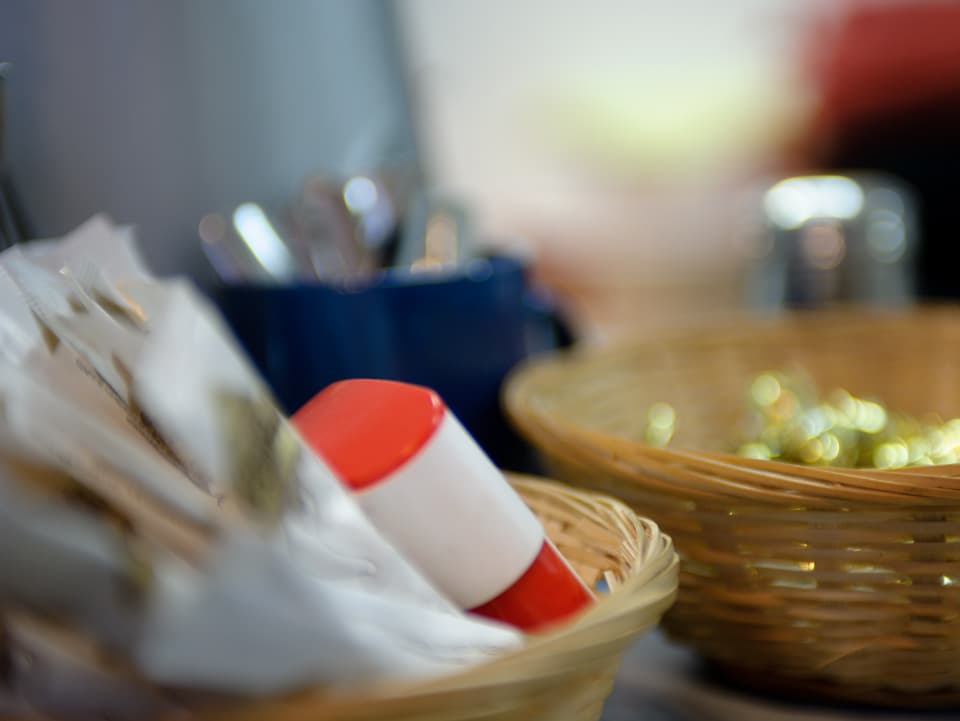 Stillleben mit zwei Körbchen, die Zucker und kleine, in Goldpapier verpackte, Süssigkeiten. Im Hintergrund eine blaue Tasse mit Teelöffeln.