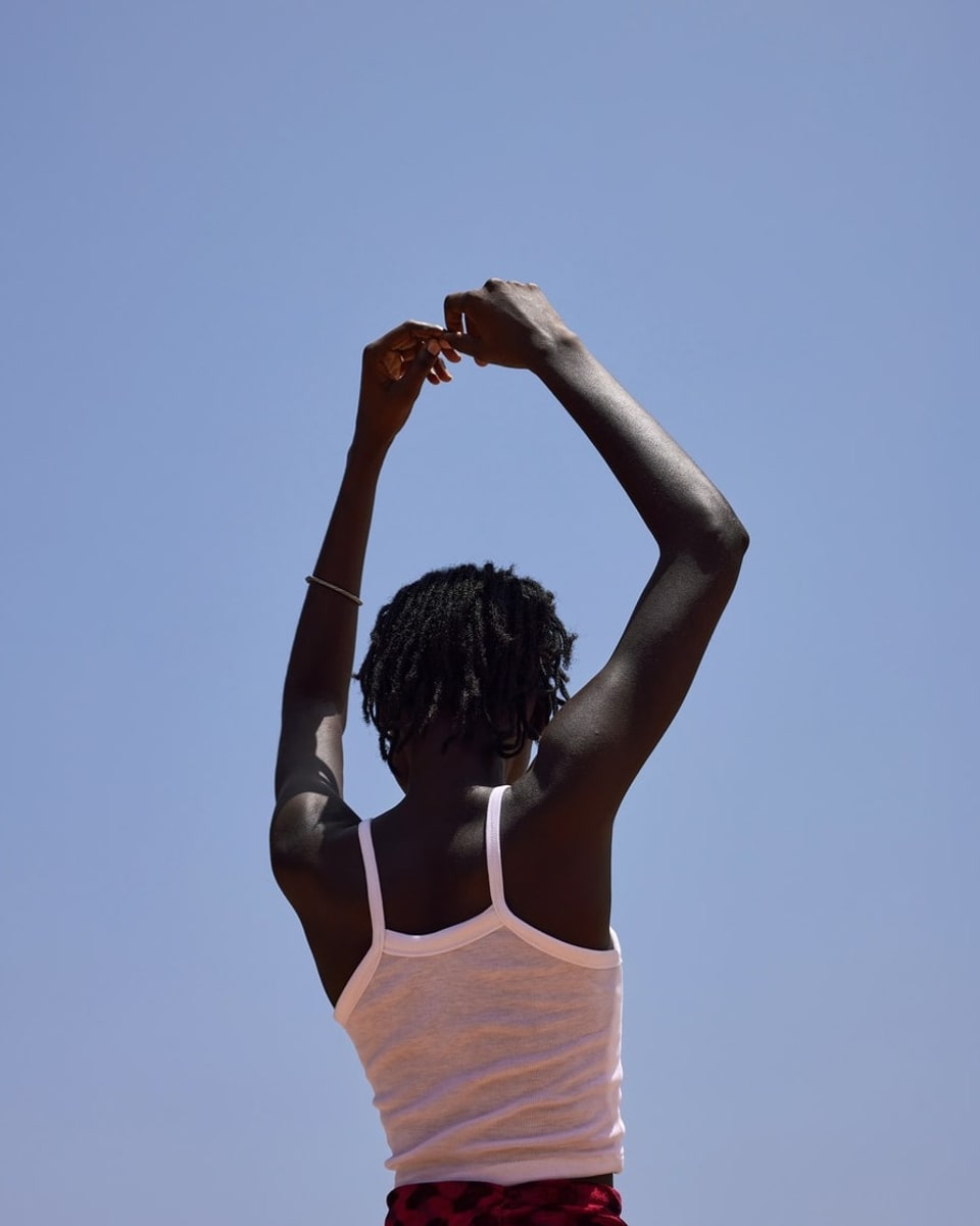 Frau aus Senegal mit weissem Shirt hält die Arme in den Himmel.