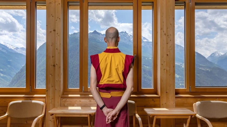 Mönch steht vor einem Fenster mit Blick auf Schweizer Berge