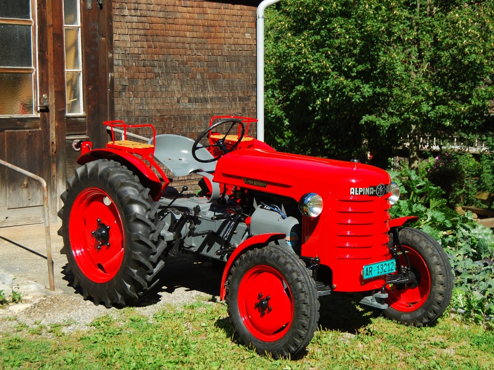 Ein roter Traktor vom Typ Alpina-Oekonom aus dem Jahr 1957 vor einem Bauernhaus.