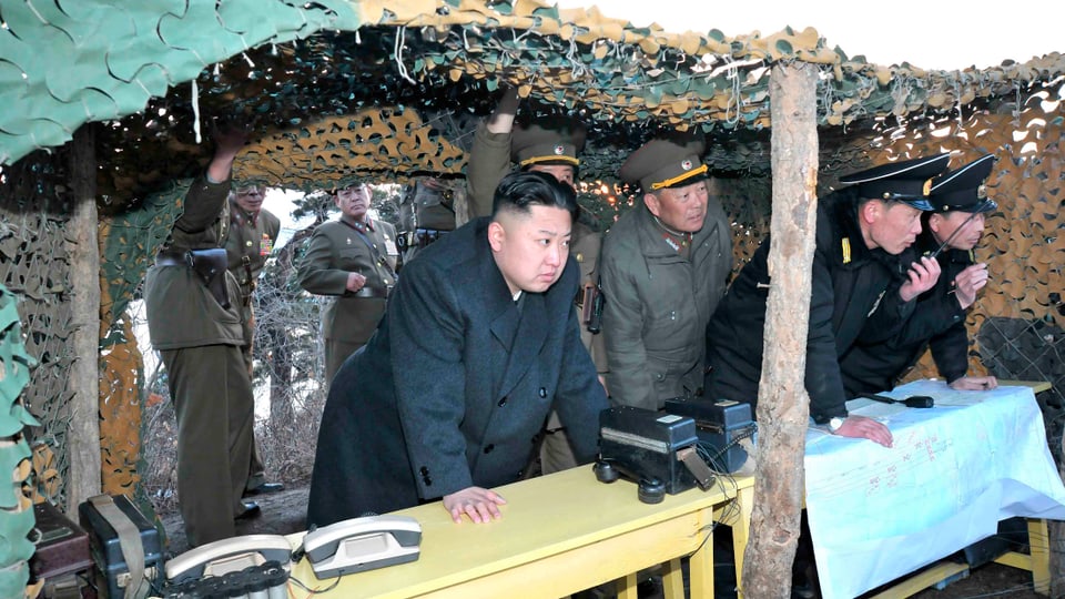 Kim Jong Un mit Militärs in einem Unterstand unter einem Tarnnetz.