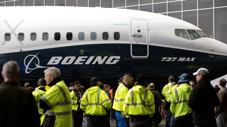 Leute in gelben Westen stehen auf einem Flugfeld vor einer Boeing 737 Max 8.