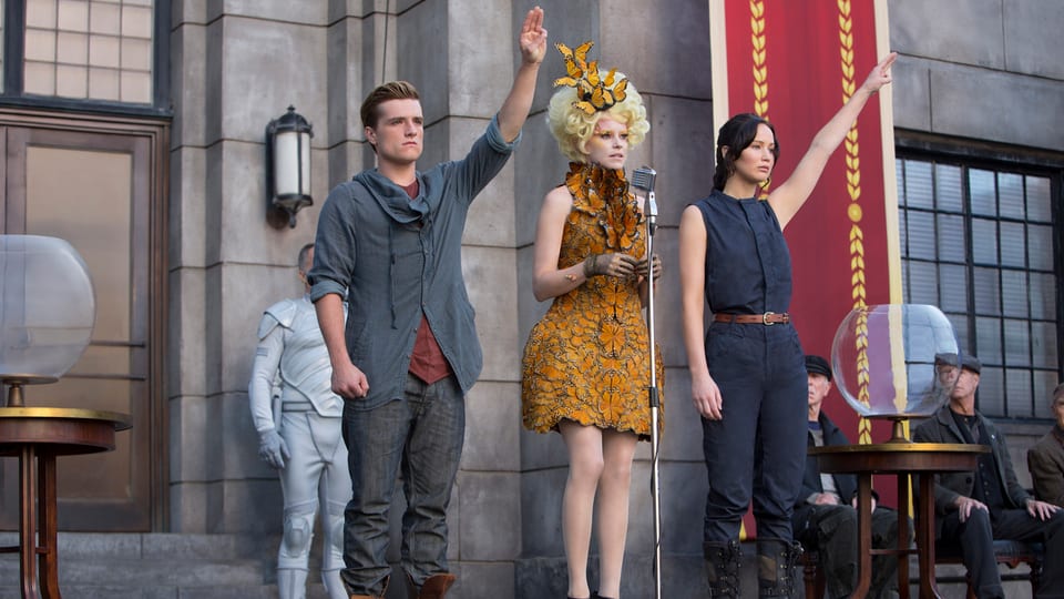 Szene aus Hunger Games, die beiden Hauptfiguren mit erhobenem linken Arm.