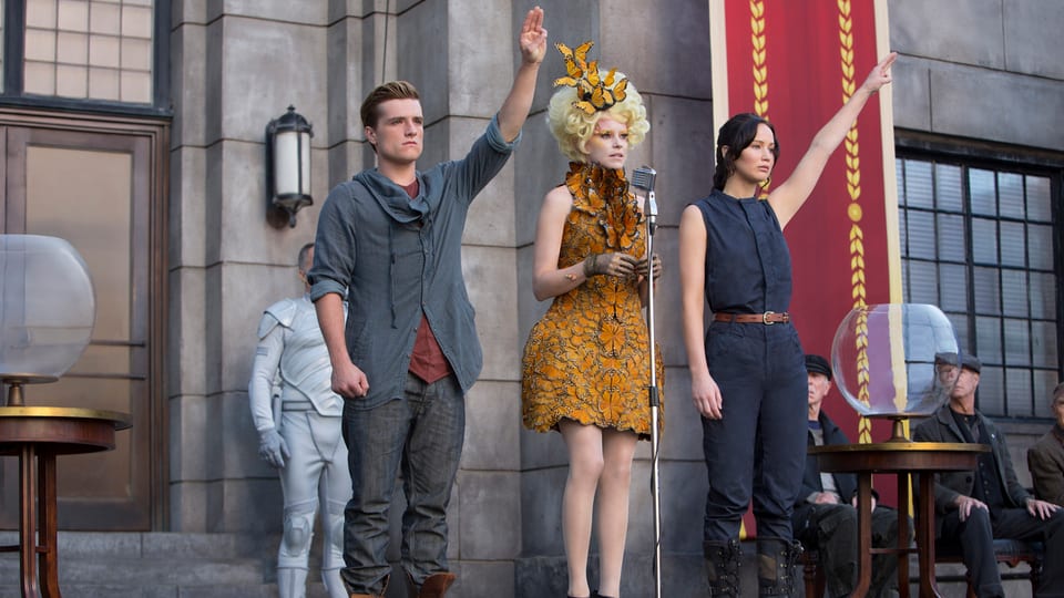 Szene aus Hunger Games, die beiden Hauptfiguren mit erhobenem linken Arm.