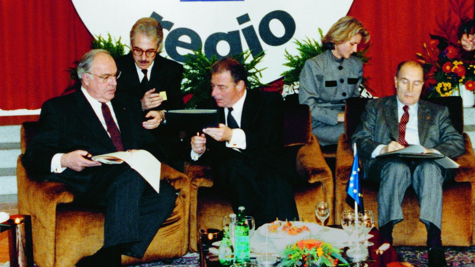 Bundeskanzler Helmut Kohl, Bundespräsident Jean-Pascal Delamuraz und Staatspräsident François Mitterand sitzen auf einer Polstergruppe.