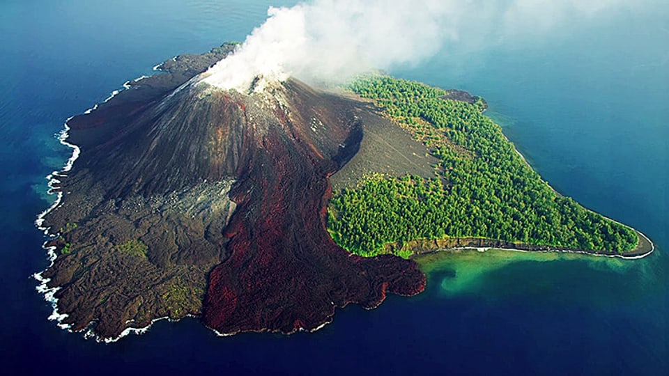 Auf einer Vulkaninsel sind unberührte Wälder, ein heisser Lavastrom und abgekühltes Lava gleichzeitig zu sehen.