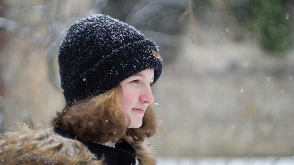Mädchen mit schwarzer Mütze steht im Schnee