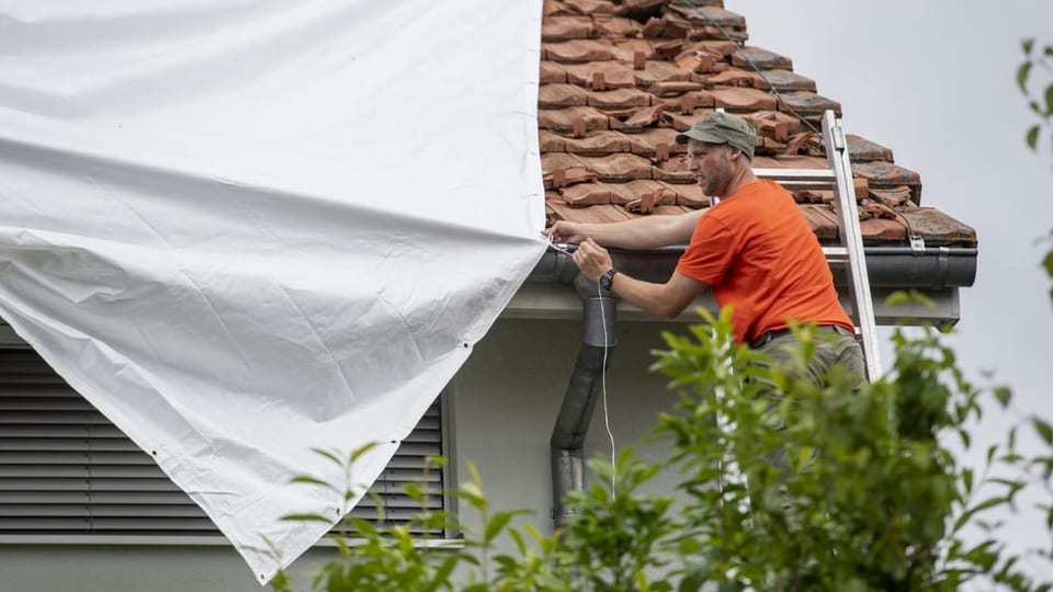 Ein Zivilschützer zieht in Wolhusen eine Plastikplane über ein beschädigtes Hausdach.