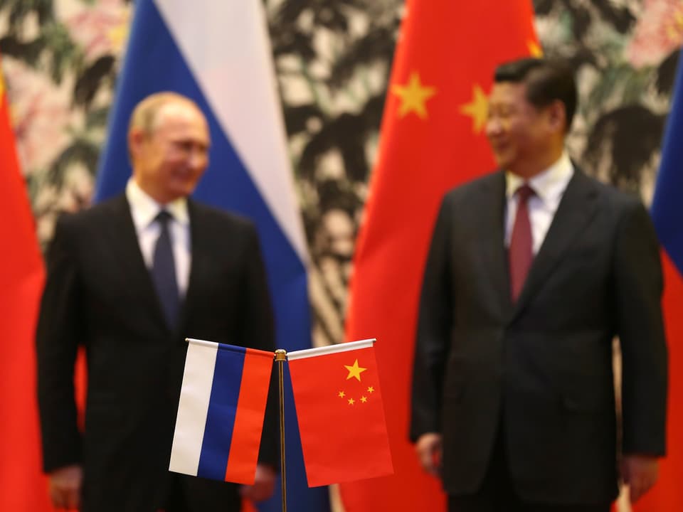 Im Vordergrund: Russische und chinesische Flagge. Dahinter: Wladimir Putin und Xi Jinping.