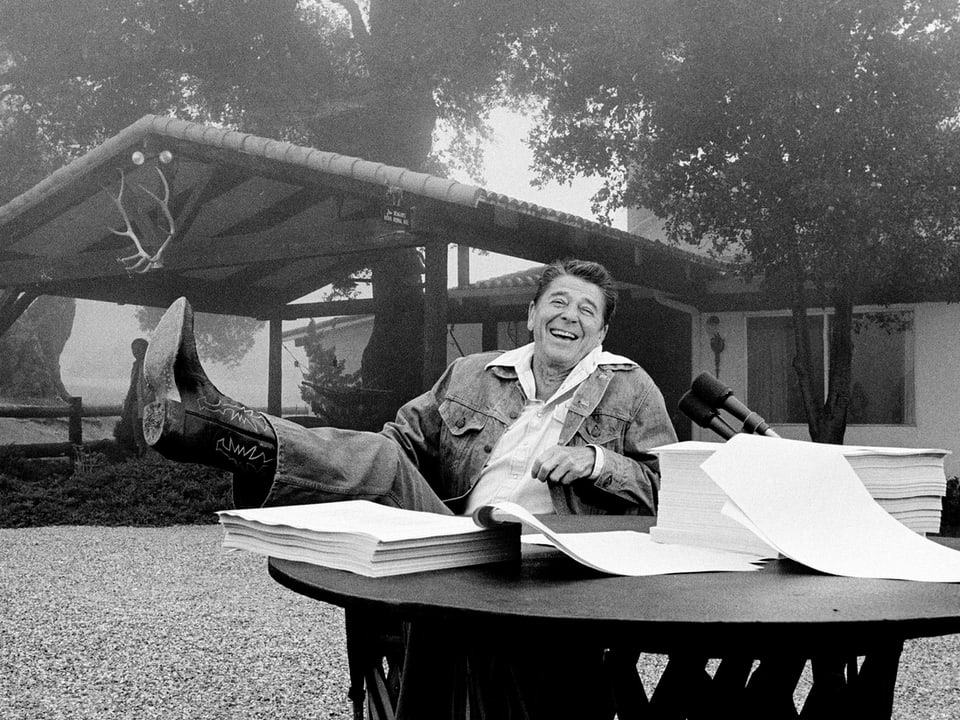 Ronald Reagan mit Stiefeln an einem Tisch voller Akten.