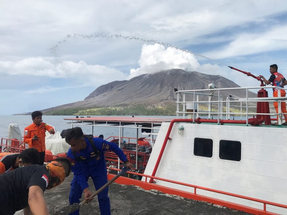Mannschaft auf einem Schiff mit einem rauchenden Vulkan im Hintergrund