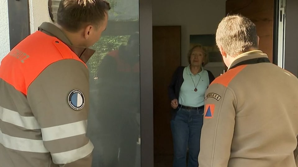 Eine Hausbesitzerin öffnet zwei Zivilschützern ihre Tür.