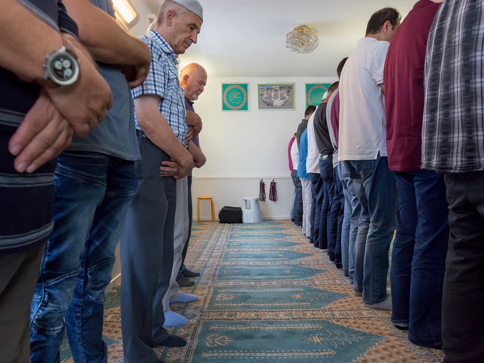 Männer stehen mit den Händen verschränkt im Gebetsraum der Moschee.