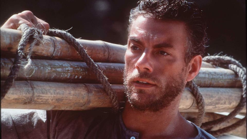 Jean Claude Van Damme mit Holz auf der Schulter.