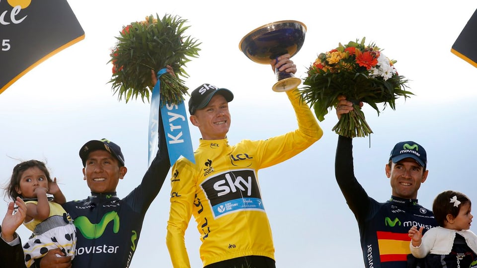 Tour-Sieger Chris Froome stemmt die Trophäe in die Höhe, daneben stehen Nairo Quintana und Alejandro Valverde, beide mit Blumenstrauss und ihren Töchtern auf dem Arm.