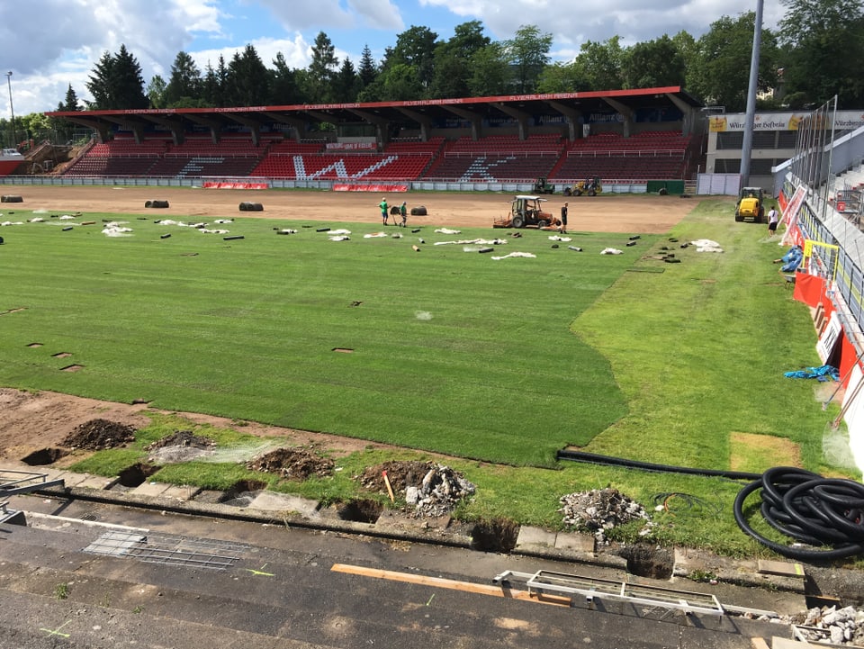 Ein Fussballstadion, in dem der Rasen am Rande aufgegraben ist. Hier werden Leitungen verlegt. 