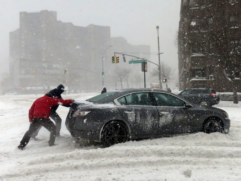 Zwei Männer stossen ein Auto, schneebedeckte Strasse