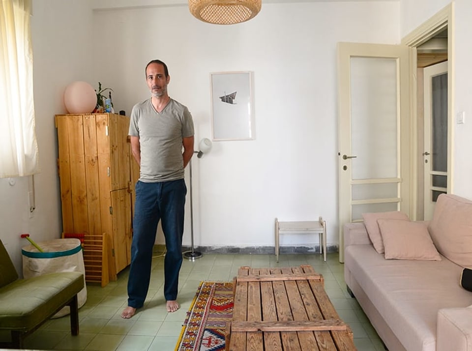 Ein Mann in blauen Hosen und grauem T-Shirt steht in einem Wohnzimmer.