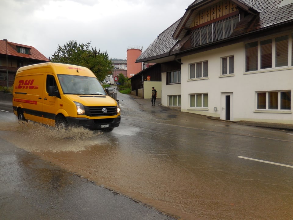 Ein DHL-Transporter fährt auf einer überfluteten Strasse. Das Wasser spritzt in alle Richtungen.