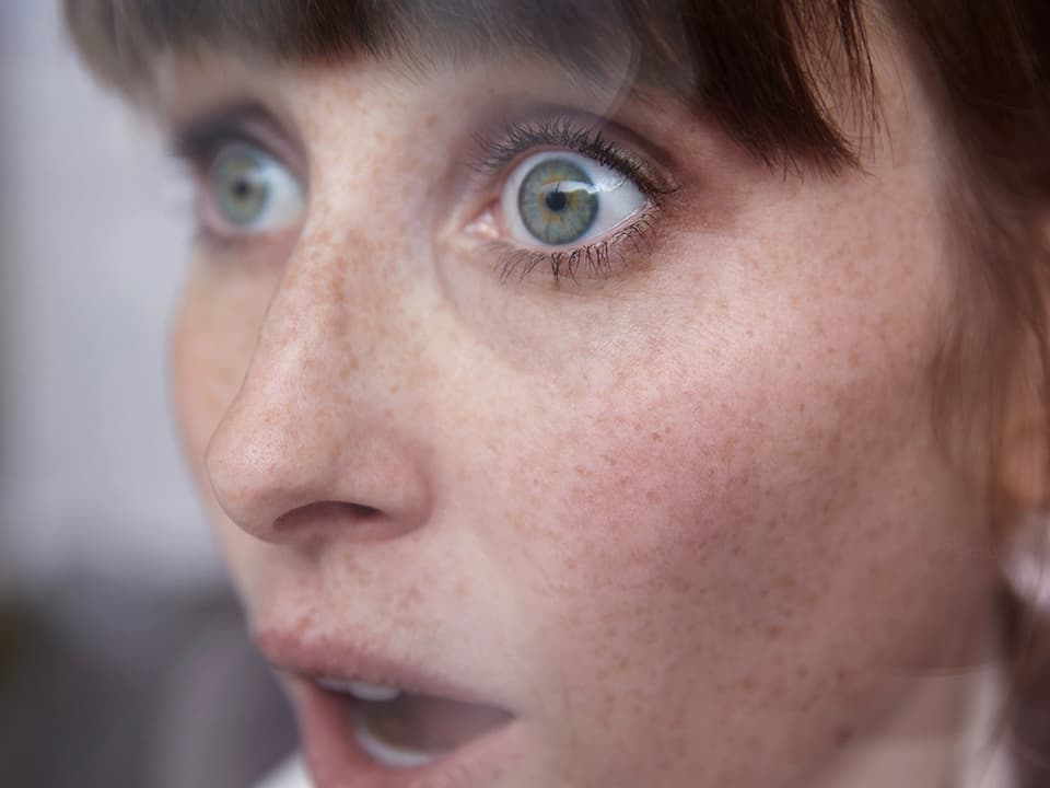 Eine Frau scheint erschrocken oder überrascht zu sein. Sie reisst die Augen auf und hat den Mund offen.