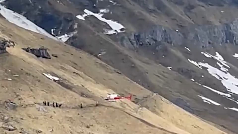 Rettungshelikopter in aperter Landschaft mit Schneeresten.
