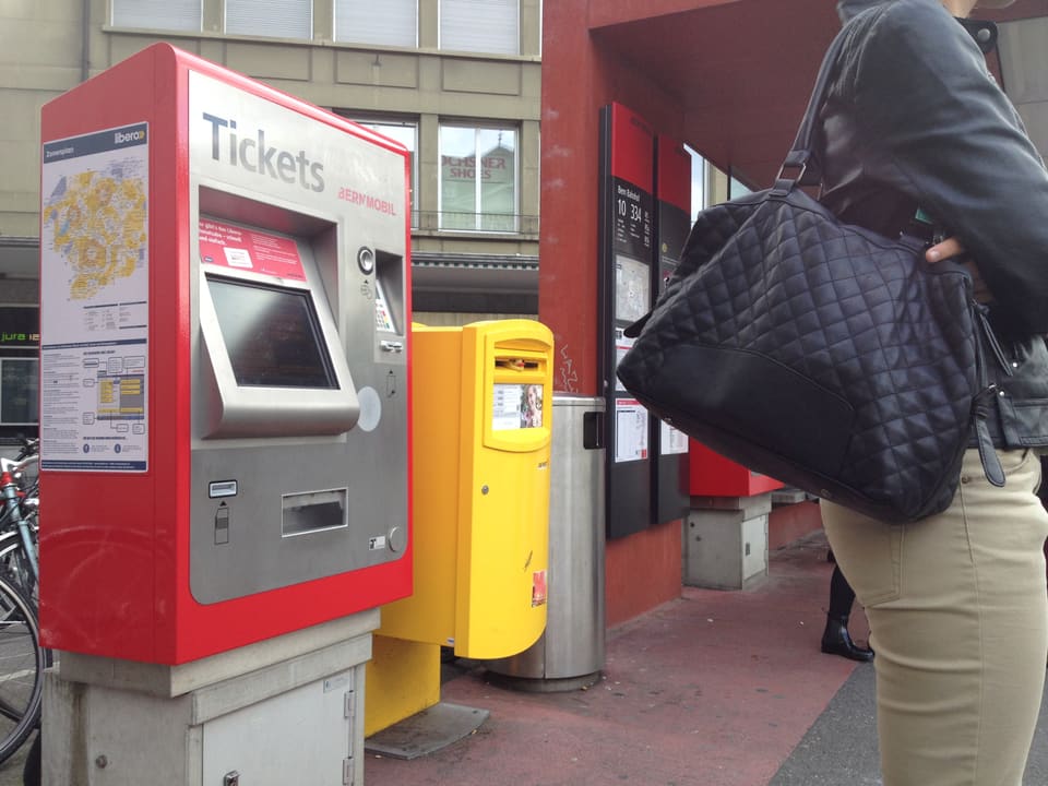 Ticketautomat für Busbillete, Postbriefkasten, wartende Frau