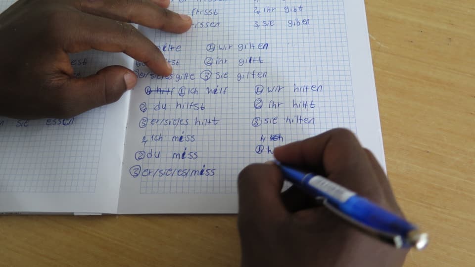 Eine Asylsuchende hält einen Stift und schreibt Verben auf.