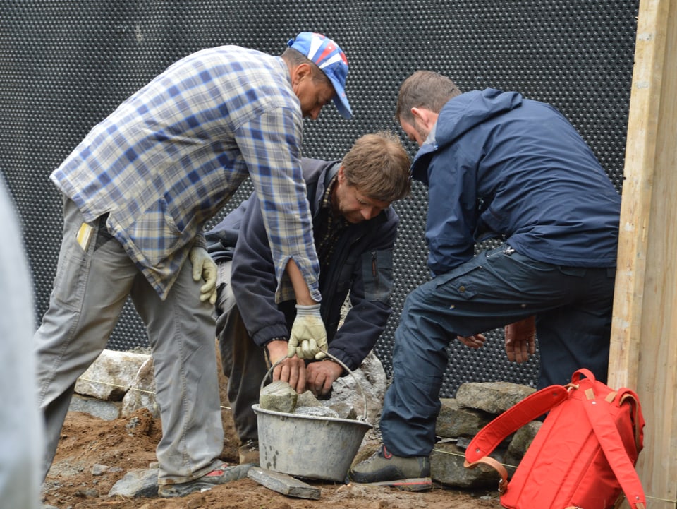 Drei Männer bearbeiten eine Trockenmauer. Einer davon Nik Hartmann. Er versucht zu helfen. 