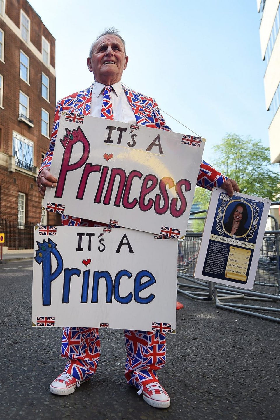 Ein Mann hält zwei Plakate, welche die Geburt einer Prinzessin oder eines Prinzen verkündet.