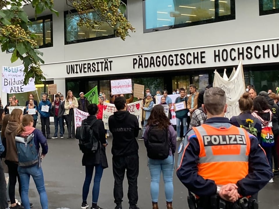 Ein Polizist beobachtet eine Gruppe Demonstranten vor der Universität Luzern.