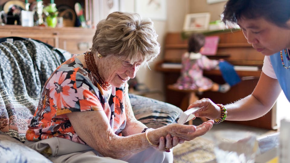 Eine Pflegefachfrau gibt einer älteren Frau Medikamente in die Hand.