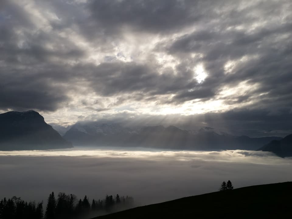 Die Sonne scheint durch eine Wolkenlücke hindurch auf den nebelgefluteten Talkessel von Schwyz.