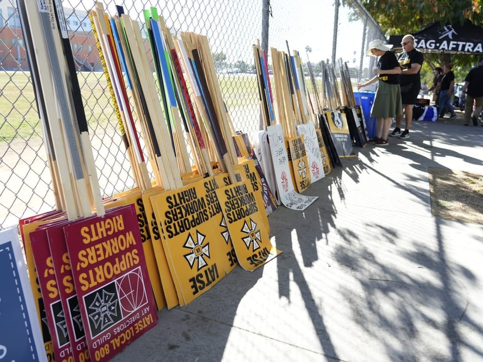 Streikplakate stehen an einen Zaun gelegt auf einem Bürgersteig.