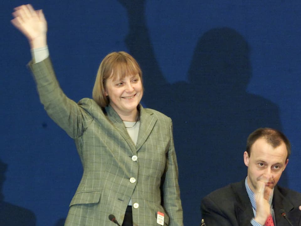 Merkel hebt triumphierend die Hand, Merz klatscht.
