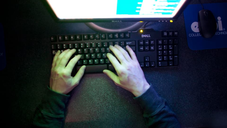 Hände eines Mannes auf einer Computertastatur vor einem Computerbildschirm