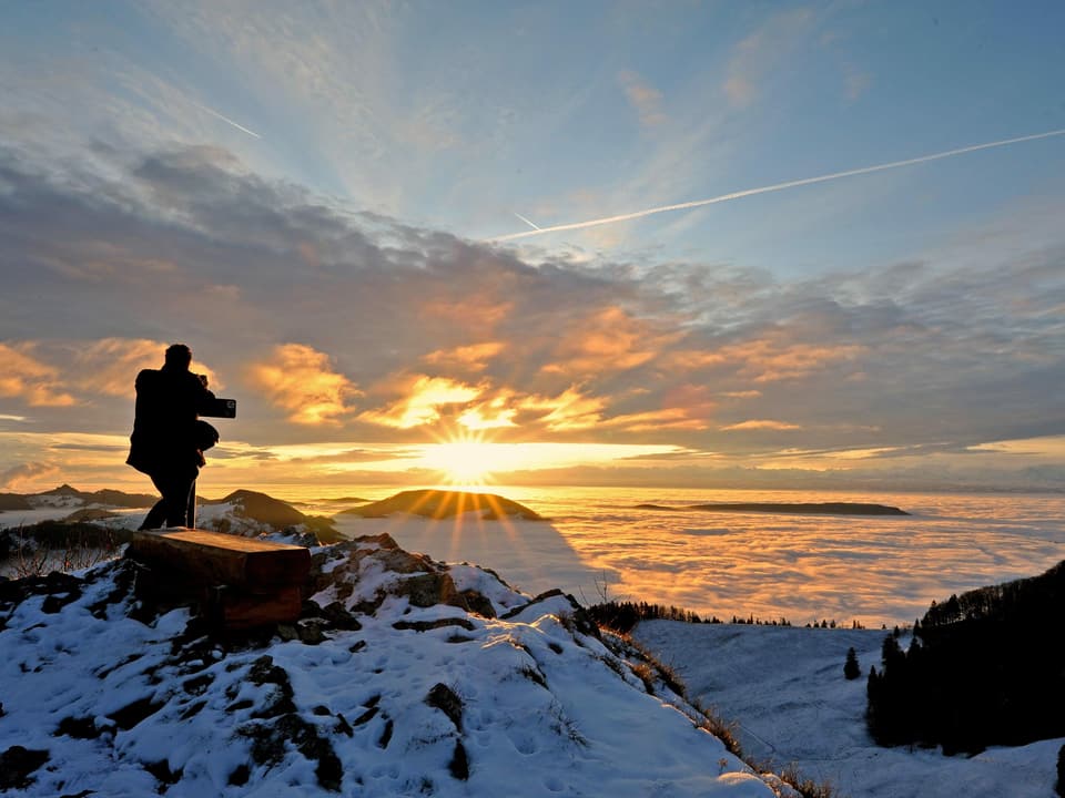 Sonnenaufgang in den verschneiten Bergen, ein Fotograf steht am Gipfel.