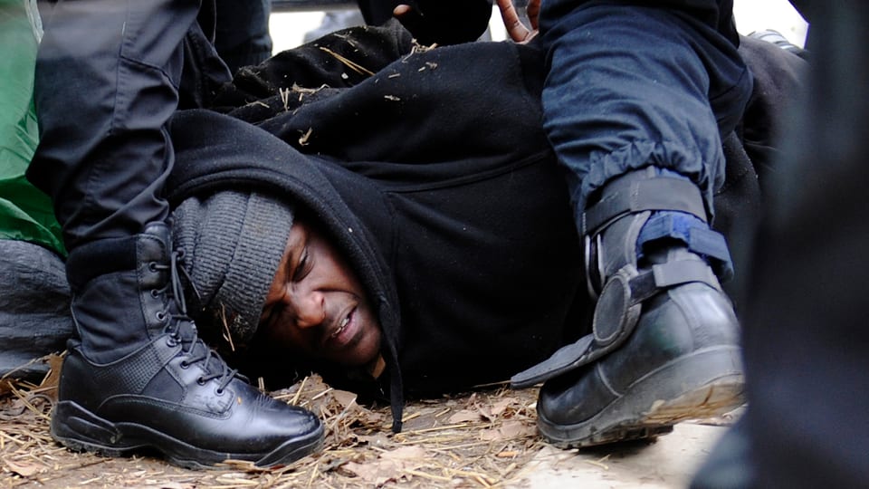 Afroamerikaner wird von Polizisten auf den Boden gedrückt, ihm werden Handschellen angelegt.