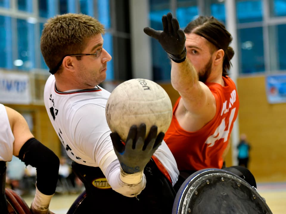 Zwei Männer spielen Rollstuhl-Rugby und kämpfen um den Spielball.