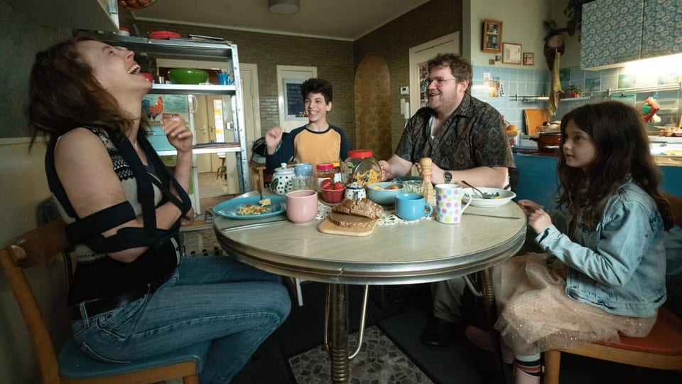 Ein Mann, eine Frau, ein Mädchen und ein Junge sitzen um einen Esstisch und lachen.