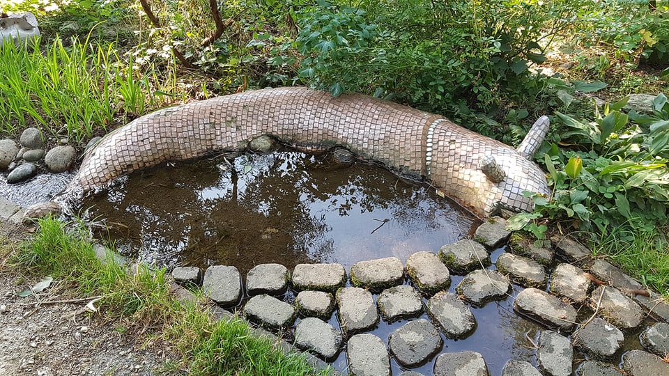 Eine Skulptur mit Mosaiksteinen umrundet einen kleinen flachen Brunnen.