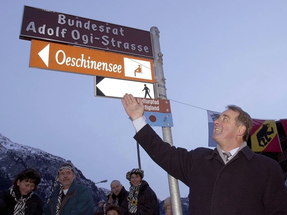 Adolf Ogi zeigt mit dem Finger auf die Strassentafel mit seinem Namen.